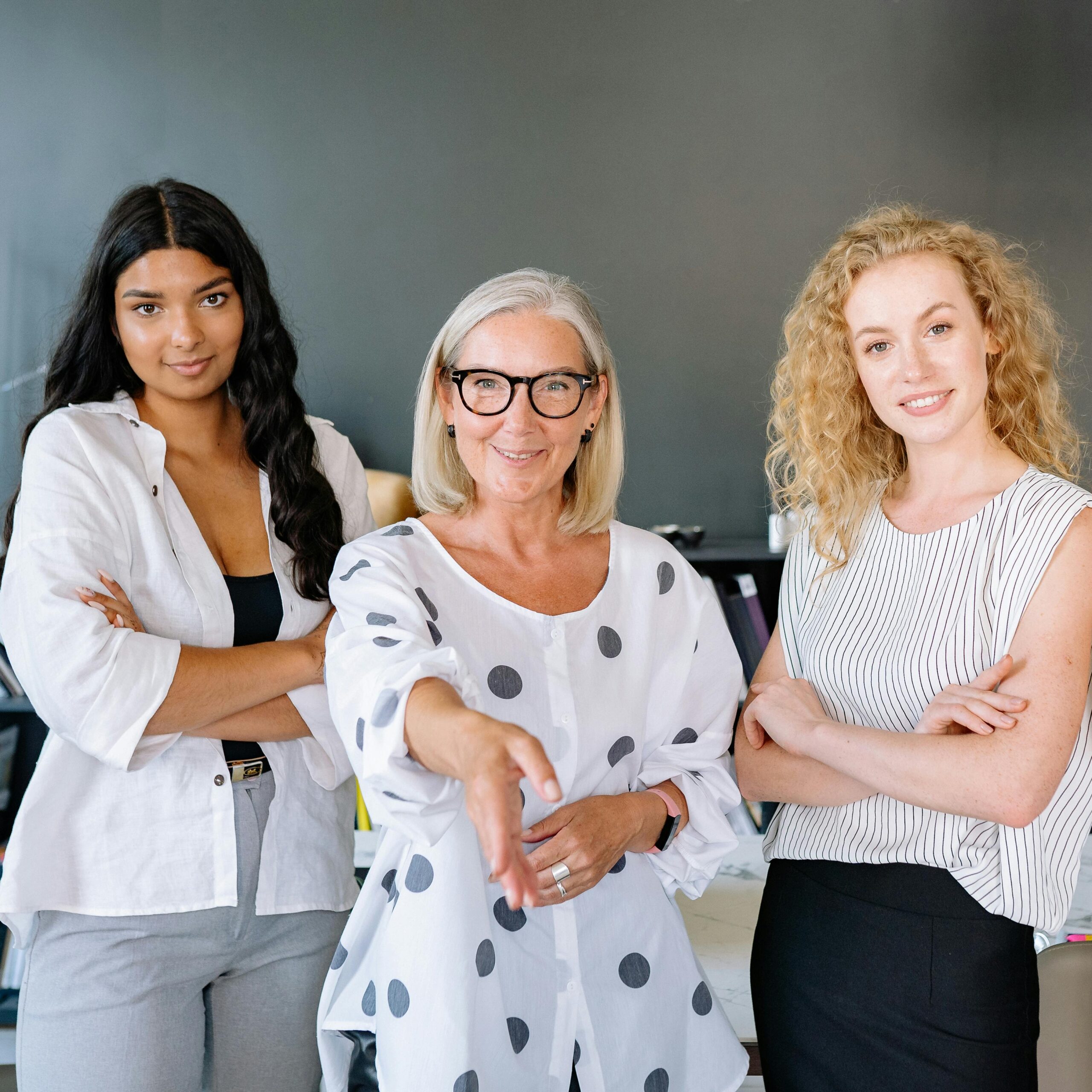 Three diverse businesswomen standing confidently in an office, showcasing teamwork and professionalism.